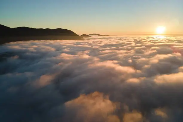 Photo of Aerial view of colorful sunrise over white dense fog with distant dark silhouettes of mountain hills on horizon