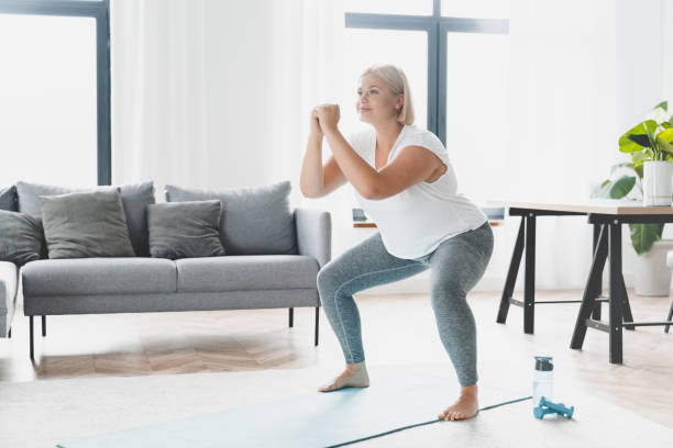 istock Plus size fat plump caucasian young woman athlete doing home workout training, losing weight, doing squats in fitness sporty clothes, slimmimg indoors 1401592383