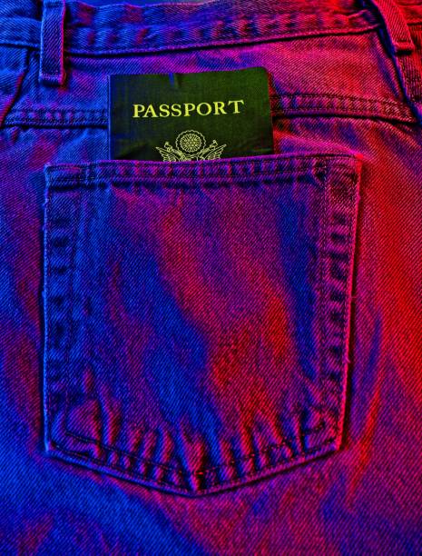 The back pocket of a pair of blue jeans with a passport sticking out of pocket, an American travel and fashion concept The back pocket of a pair of blue jeans light painted with red and blue light and passport. An American fashion influence concept. Texture of jean fabric highlighted with red and blue side light, an abstract background object with room for copy. jeans denim passport pocket stock pictures, royalty-free photos & images