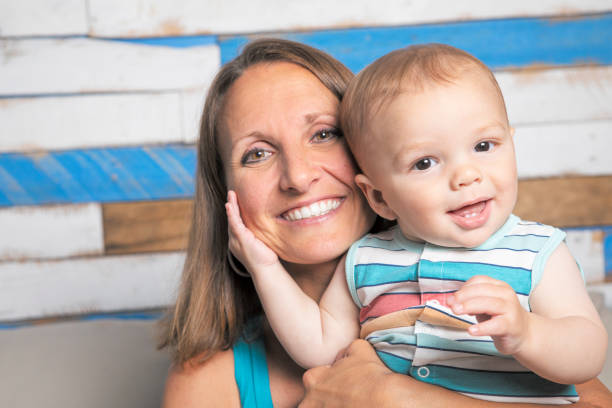 A 9 month old baby boy smiling as he hugs his mother's head.