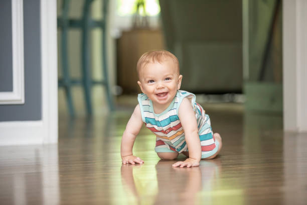 Happy Nine Month Old Baby Boy Crawling on Floor A 9 month old baby boy smiling as he crawls on the hardwood floors of his home. baby teeth stock pictures, royalty-free photos & images