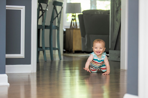 A 9 month old baby boy smiling and laughing as he crawls toward the camera.