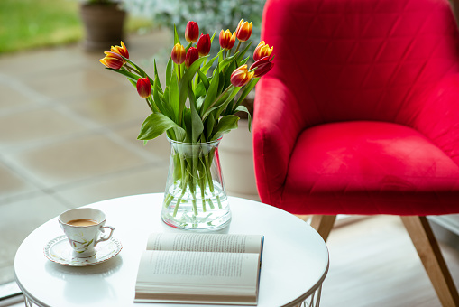 Fresh spring tulips in glass vase and a cup of coffee with a book for reading