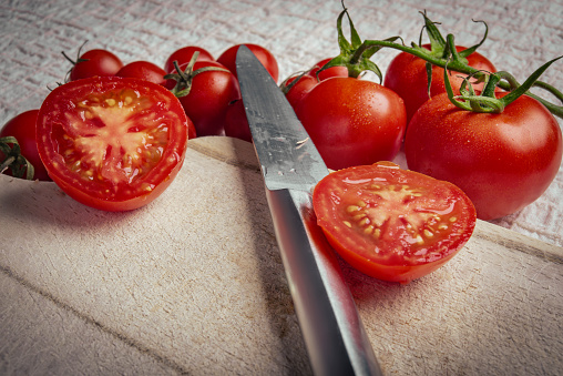 A slice of red juicy tomatoes and a sharp chef's knife on a cutting board in the kitchen