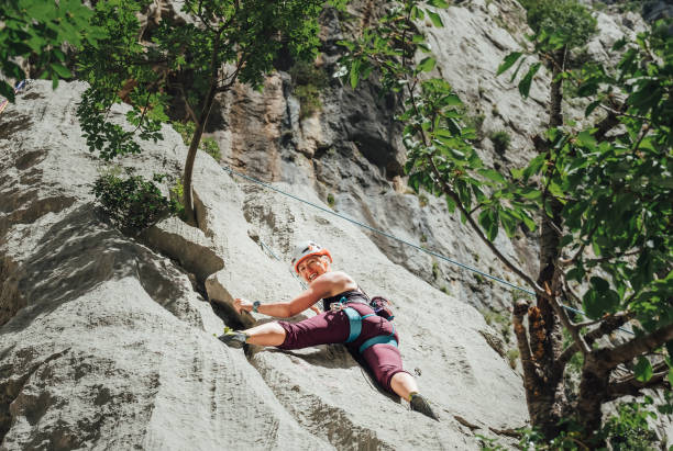 istock Smiling athletic woman in protective helmet climbing cliff rock wall using top rope and climbing harness in Paklenica National park site in Croatia. Active extreme sports time spending concept. 1401601247