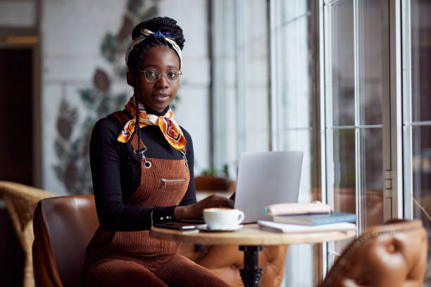 Portrait of an african college girl sits in a cafeteria and typing on a laptop. stock photo