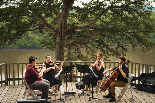 String quartet of two young men and two young women playing concert on wooden deck above Missouri River on summer evening