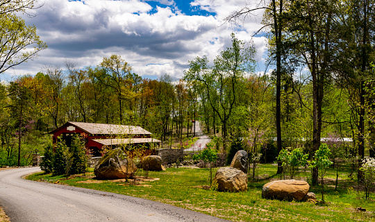 View of a Country Road Approaching to a Restored Covered Bridge on a Sunny Spring Day