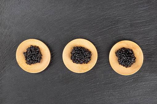 Top view of wooden mini plates with black caviar on a stone background. Copy space.