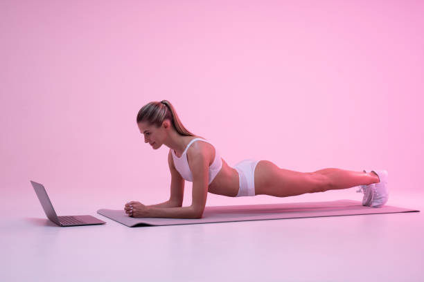 istock Young woman in neon light standing in plank position, watching online workout tutorial on laptop 1401606604