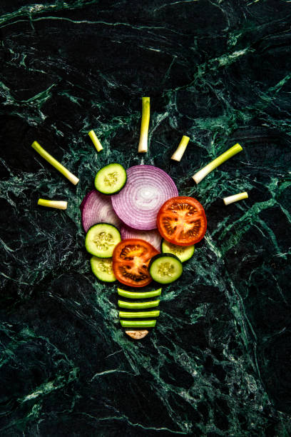 This is a conceptual photo related to the great idea of healthy eating using tomatoes, cucumbers, onions, and turnips and shaping them into the form of a lightbulb on a green dark marble kitchen countertop