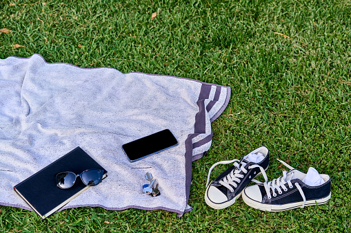Towel in the grass pool with summer kit book and glasses smartphone and shoes