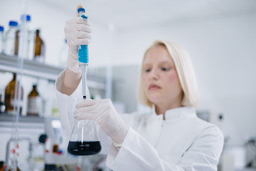 Blonde young female scientist wearing a lab coat, working in her laboratory and experimenting with diverse set of liquids