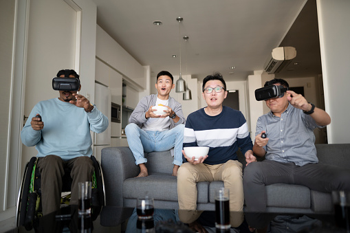 group Asian friends play VR video games together at living room sitting on sofa