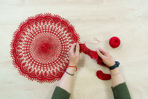 Hands of a craftswoman with a ball of red threads. Unusual hobby crochet. Background with copy space for text