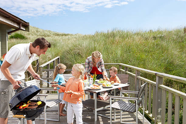 Family on vacation having barbecue Family on vacation having barbecue next to sand dunes on decking family bbq beach stock pictures, royalty-free photos & images