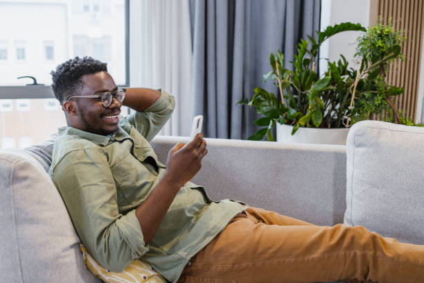 istock Smiling young man is relaxing at home and using mobile phone 1401621014