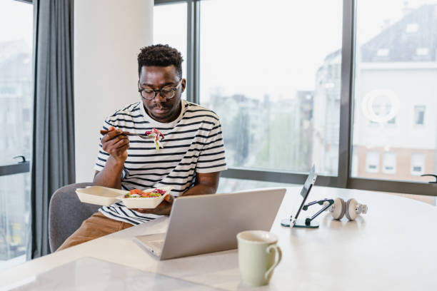 istock Multitasking young man using laptop in living room while having lunch 1401621146
