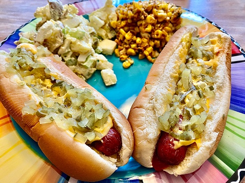 Two loaded hotdogs with potato salad and Mexican corn sides.