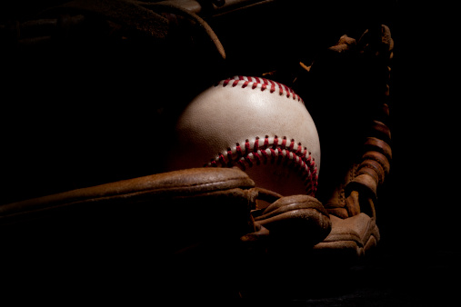 Macro shot of worn baseball and glove isolated on a black background.