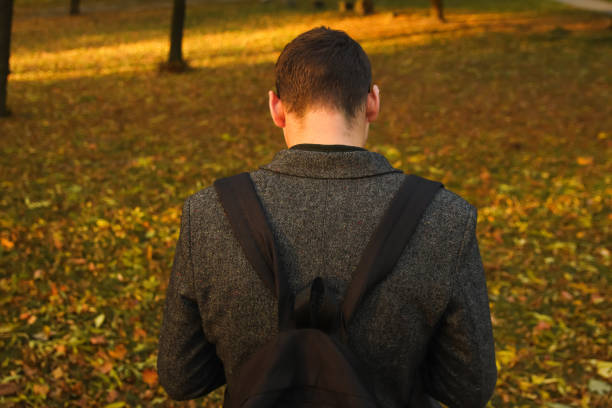 Defocus young man holding phone. Man using smart phone in autumn park. Typing text message or reading social media at mobile phone. Fall background. Cell phone. Back view. Rear. Out of focus.