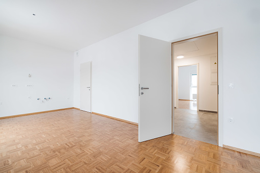 Empty room with white walls and wood flooring in a newly build public housing apartments. Bright white room with lots of natural light. Newly build modern home.