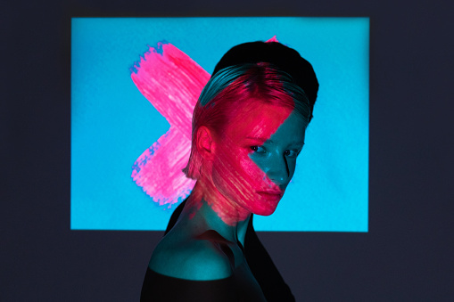 fashion androgyne woman with projection of neon pink cross shape on her face