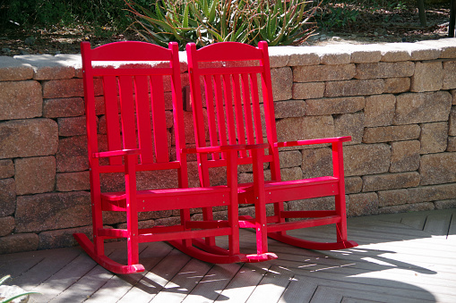 Two empty wooden red rocking chairs side by side in the sun