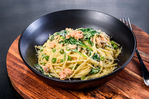 A serving of Salmon Spaghetti in a dark round bowl on a wooden background