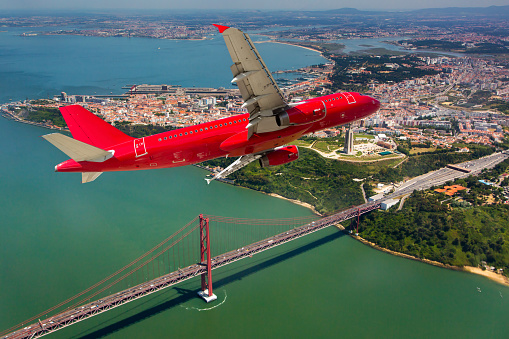 Red passenger airplane in flight. Aircraft flies against a background of city, river and bridge.