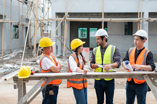 Multiethnic diverse group of engineers or business partners at construction site, working together on building's blueprint, architect industry or teamwork concept.