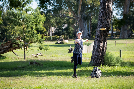 A young female disk golfer lines up her next challenging shot through the forest towards the disk golf cage