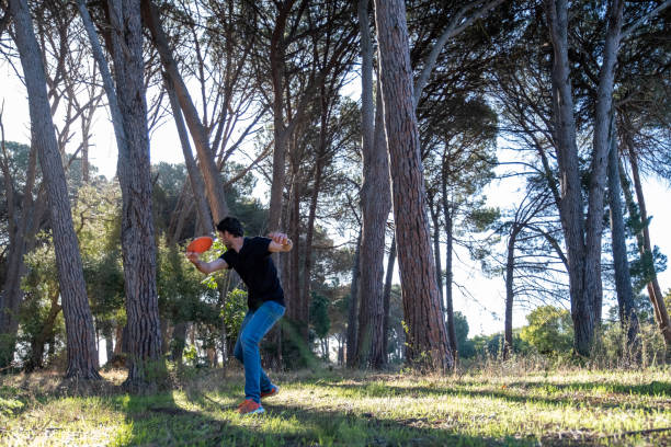 Disk golfer throws a right handed forehand through a gap in the trees stock photo