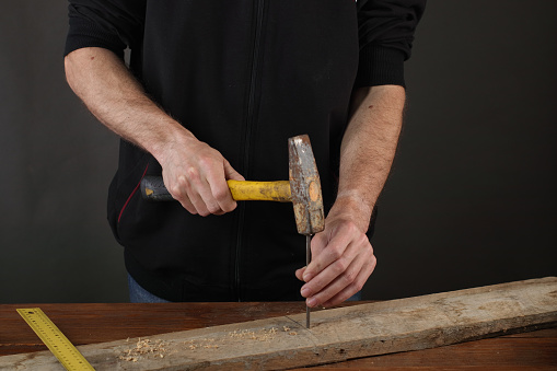 hammering a nail in a plank on a gray background