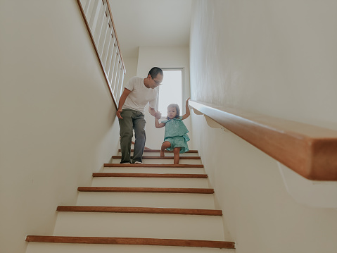 Thai father holding his daughter hand while she practicing walking down stairs by herself.