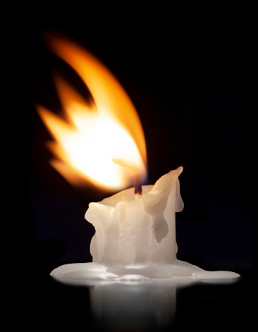 Stock photo showing elevated view of lit diya (oil lamp), with flickering flame in the dark, part of Diwali festival of lights celebration.