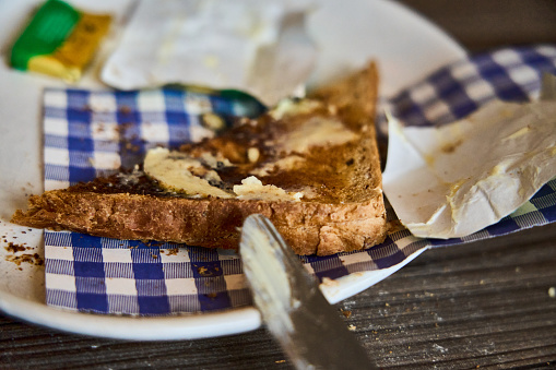 A slice of toast with butter being spread.