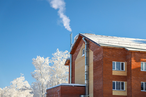 Red brick chimney with iron chimney cap on the roof in snow.