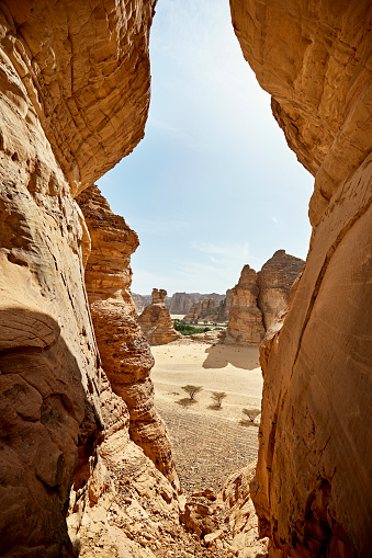 Elevated view through famous sandstone rock formation resembling a jar, bottle, or bowling pin to desert area and oasis in background.