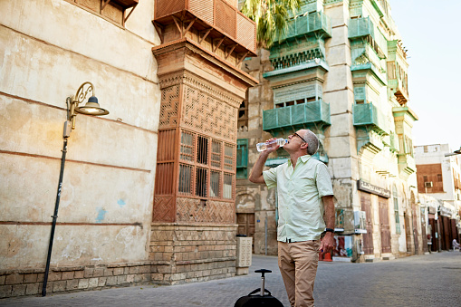 Caucasian man in mid 50s pausing to drink water while visiting Al-Balad, historic district in Jeddah, Saudi Arabia, known for its vernacular architecture.
