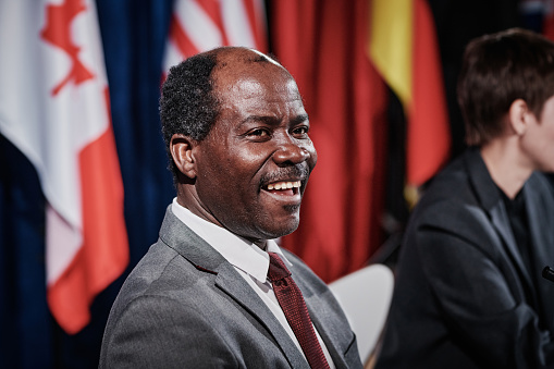 African American politician in suit laughing while sitting at international meeting with colleagues