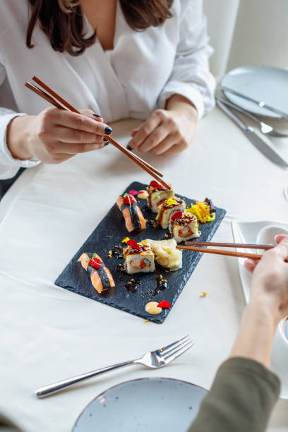 istock High angle view on hands using chopsticks and taking sushi from plate in restaurant 1401672735