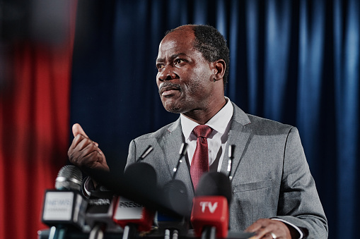 African American mature businessman in suit speaking behind the podium during his interview for television