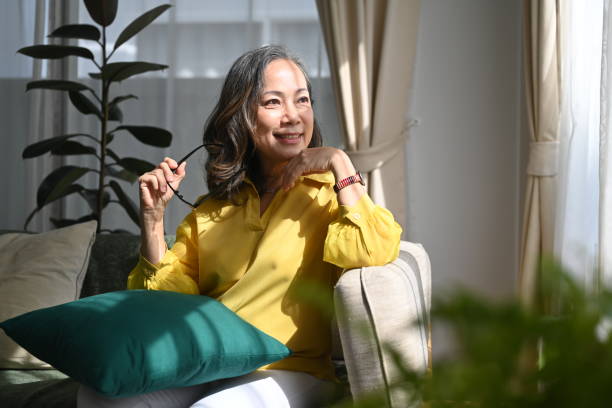istock Retired woman holding eyeglasses and looking through the window while resting sofa at home. 1401676478