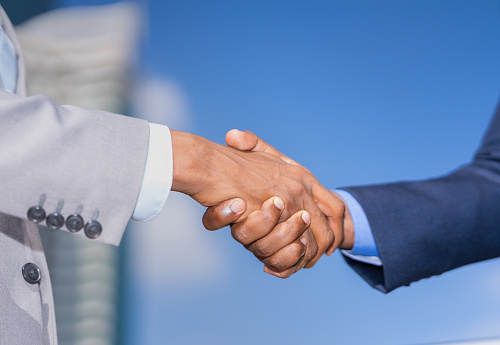 hand shake of businessman outside building in city after success business agreement. black men in grey and blue suit. building and blue sky at background