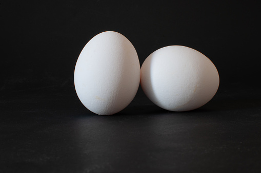 Two eggs, profile view of white raw chicken eggs isolated on dark background, selective focus.