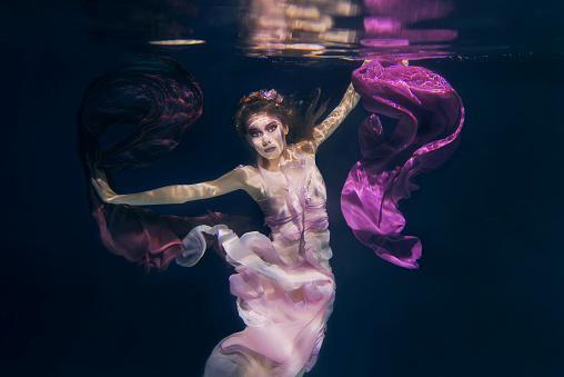 woman in colorful clothes on the dark background swimming underwater