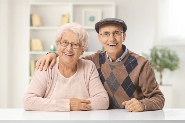istock Elderly couple sitting at a table at home and smiling at the camera 1401687752