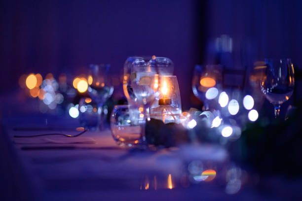 Empty Purple Restaurant place settings on table with candles cutlery and Wine Glasses at night stock photo