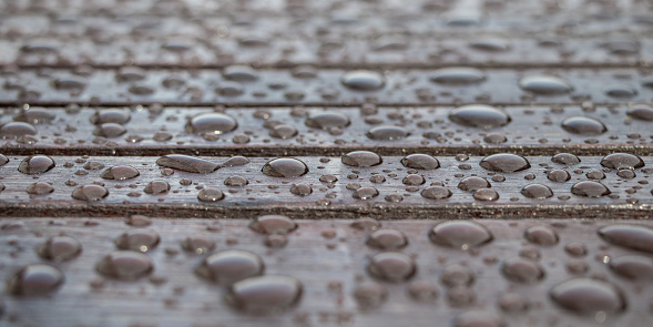 Wooden planks covered by water drops, background for rainy weather. Wet brown boards close up. Rain drops on the wooden table after rain. Selective focus